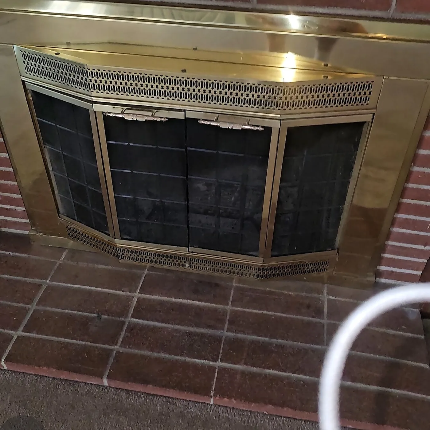Polished brass fireplace doors with mesh screens on a brick hearth