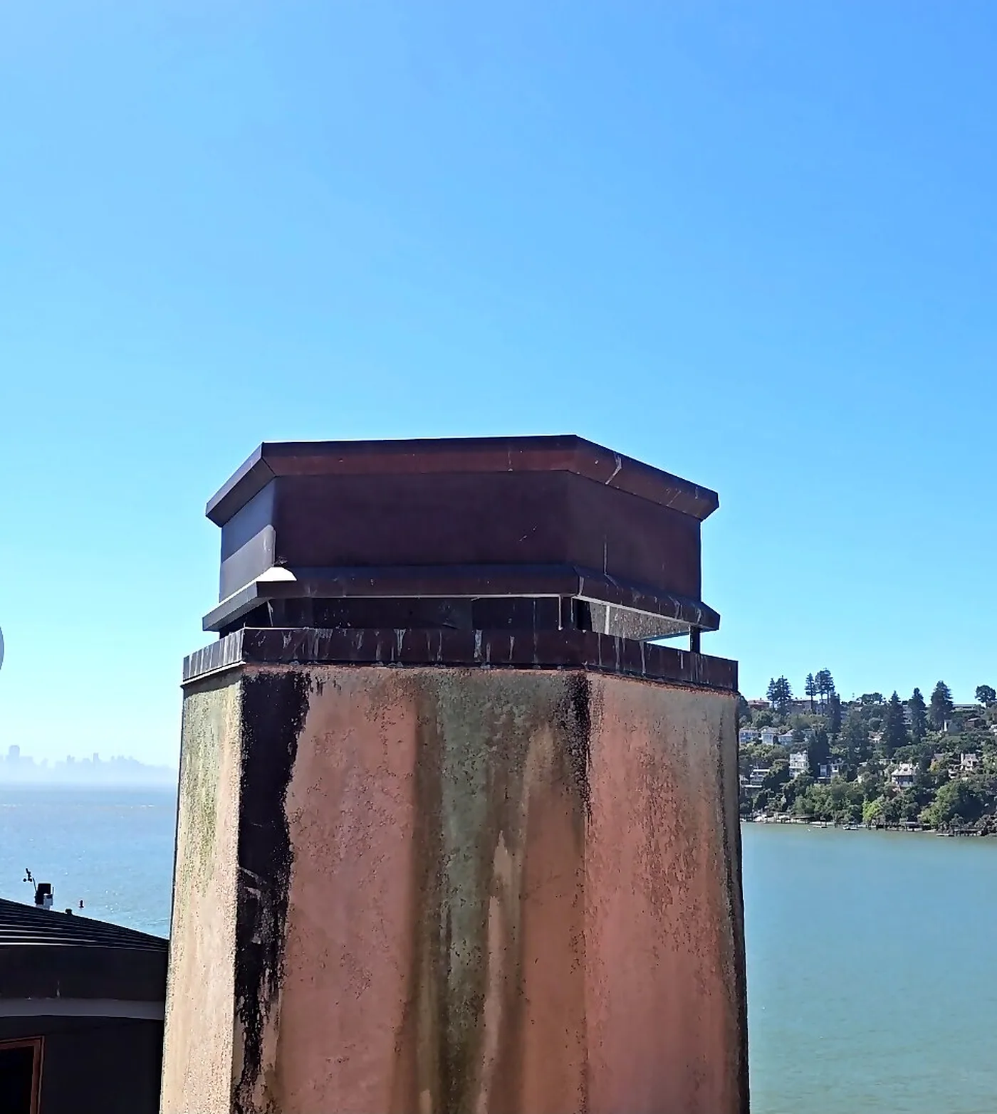 Stucco chimney with custom metal cap in Marin County with San Francisco Bay and skyline behind