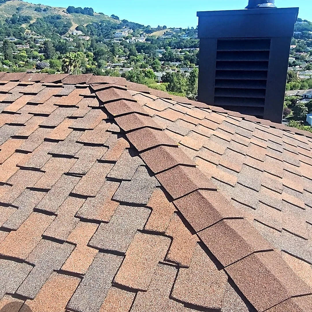 Dark chimney with louvered cap on a shingle roof ridge with North Bay hills behind