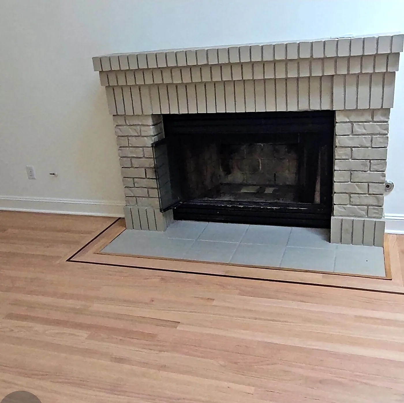Freshly cleaned firebox in a white painted brick fireplace with wood floors