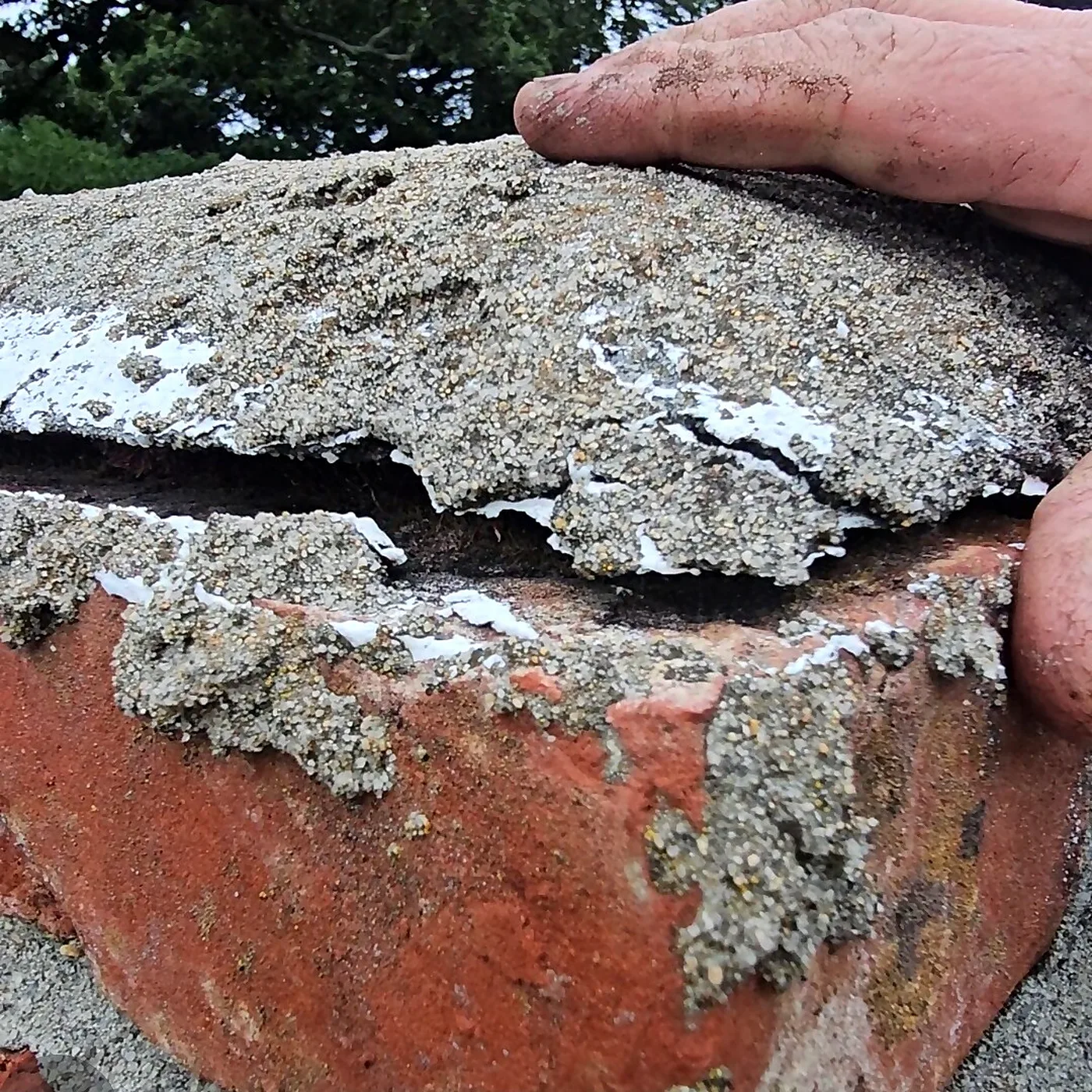 Technician hand pointing to a large crack in a chimney crown with spalling mortar