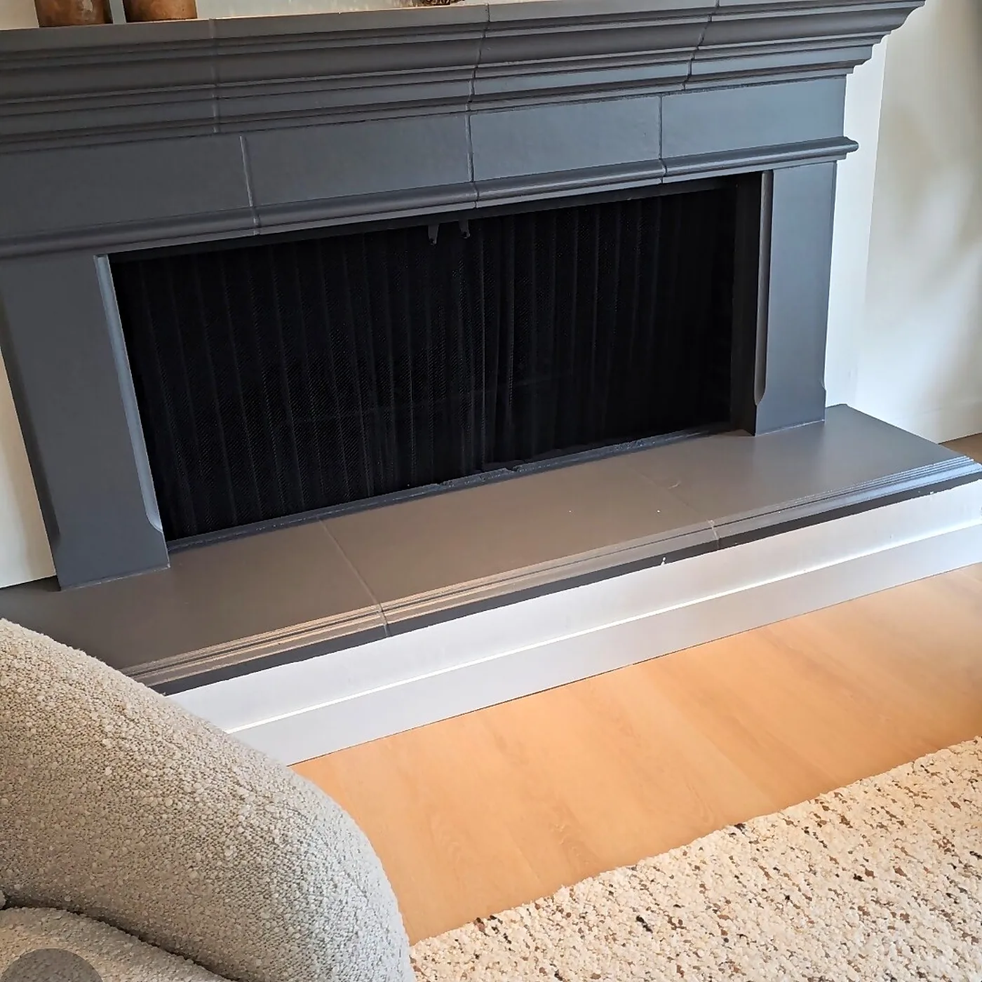 Gray painted fireplace mantel with a dark firebox and light wood floors