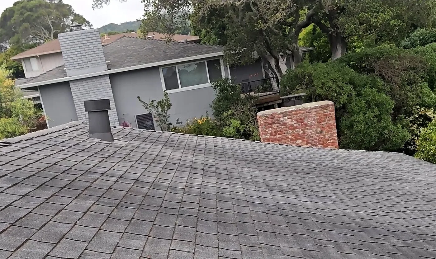 View across a gray shingle roof toward a brick chimney on an overcast day