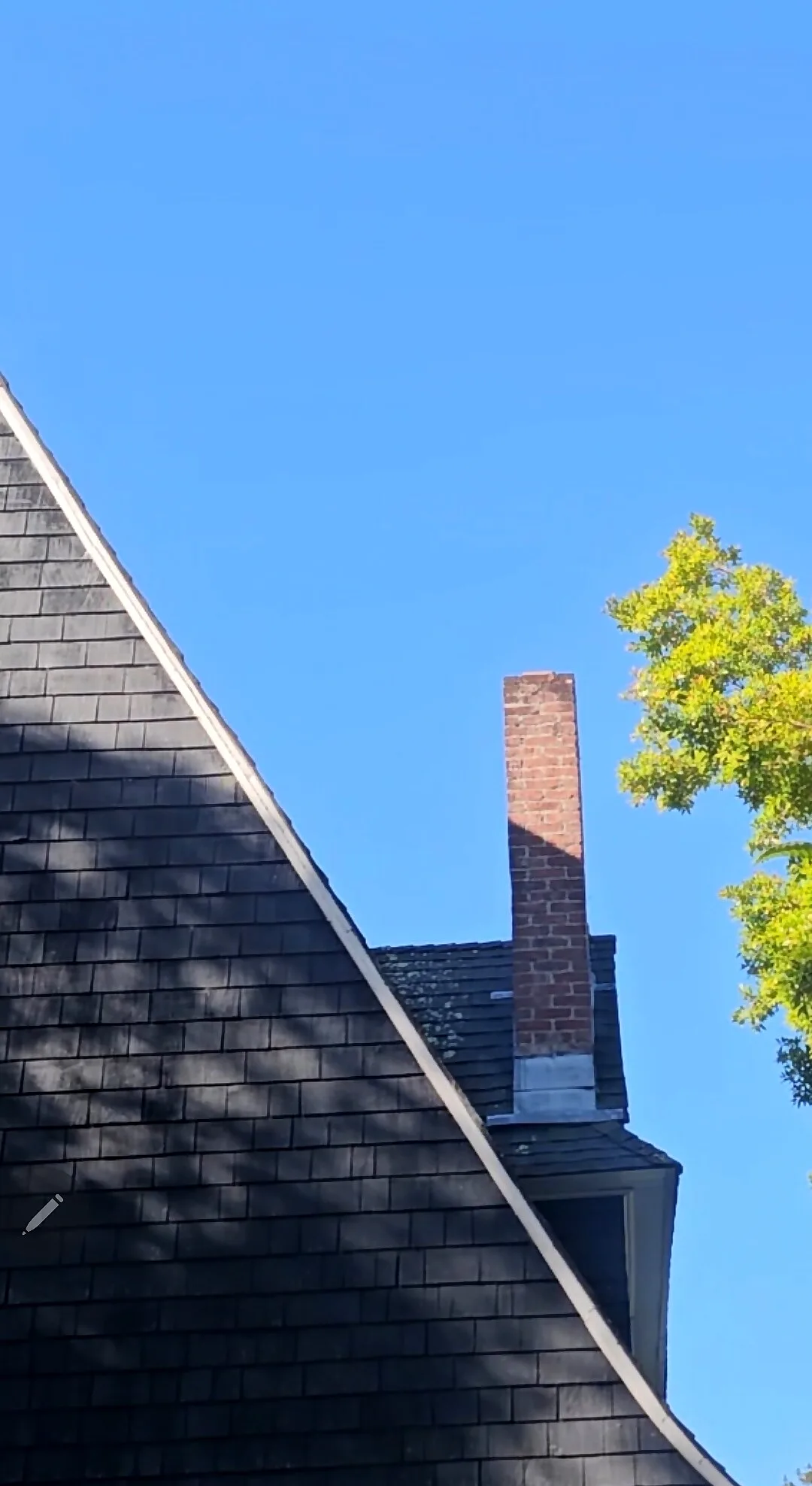 Steep dark shingle roof with a tall red brick chimney against a blue sky