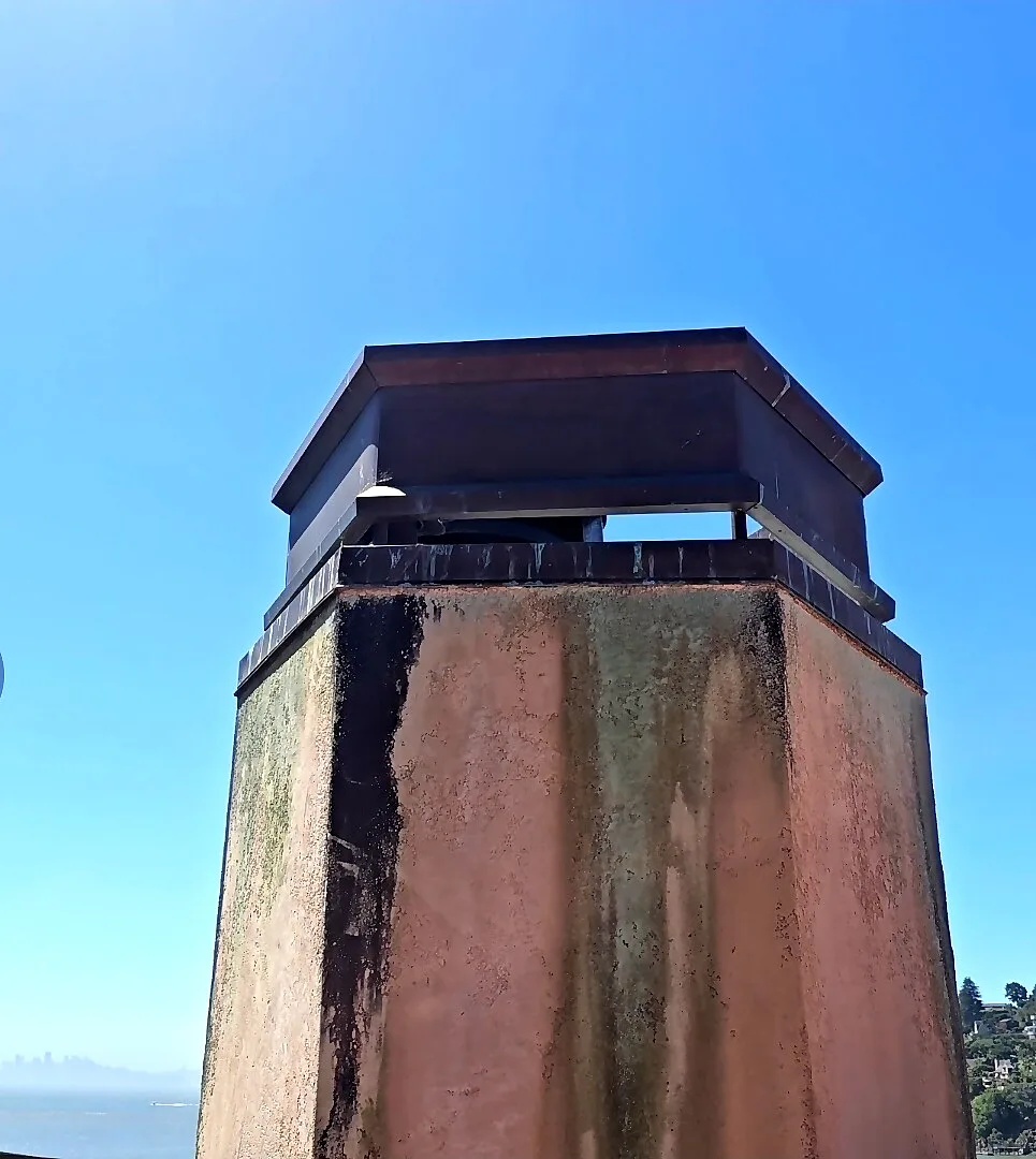 Tall tapered stucco chimney with a custom metal cap overlooking San Francisco Bay