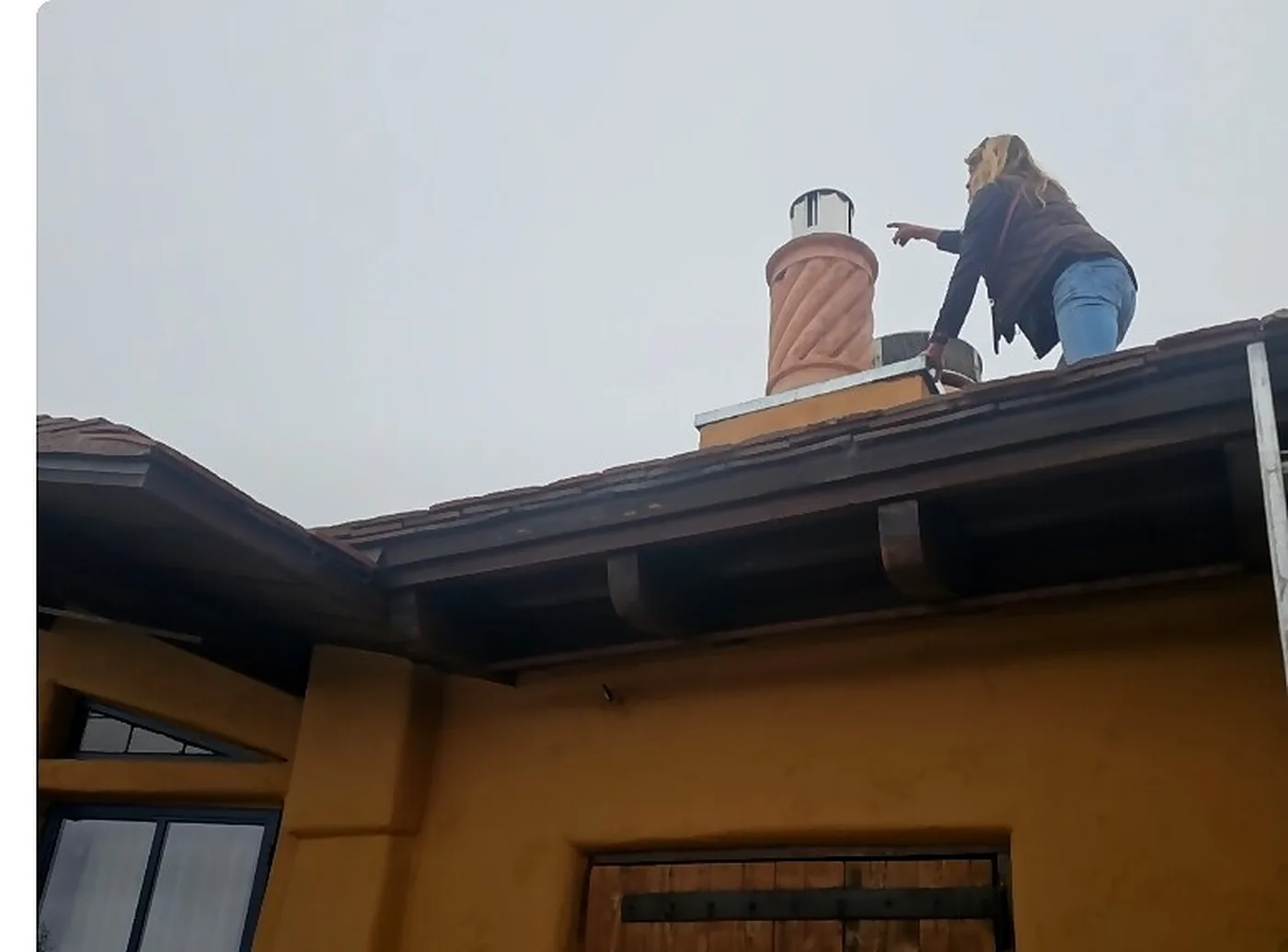 Heart's Chimney technician on a roof inspecting a terracotta chimney with a stainless cap