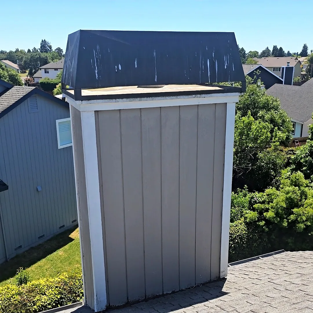 Wood-framed chimney chase with a black metal chase cover on a shingle roof